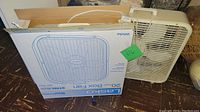 Lasko 20-inch box fan in original box next to a white ventilating fan with metal grill.