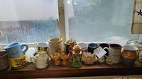 Front view of assorted mugs and decorative ceramic items arranged on a windowsill