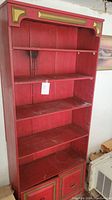 Full view of a tall red-painted wooden bookcase with visible wear and water damage on shelves and back panel.