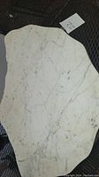 Photo of a large, irregular shaped white marble piece with grey veining and some staining, placed on a dark mesh surface.