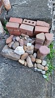 Photo showing a collection of red bricks, red clay pavers of various shapes, and an assortment of natural stones on outdoor concrete steps.