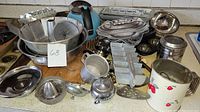 Overview of lot showing various vintage aluminum kitchen items including dishes, trays, juicer, muffin molds, kettle, and other containers on countertop