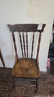 Front view of the vintage wooden chair showing carved backrest and worn wooden seat.
