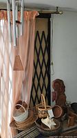 Wind chime hanging in front of peach colored curtains with some baskets and wooden decorative items placed below.