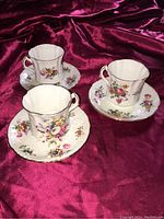 Three vintage Hammersley teacup sets with matching saucers, floral pattern and gold trim, placed on a purple velvet fabric.