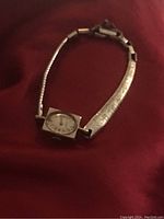 Front view of antique 14k gold watch laid on red fabric backdrop showing rectangular watch face and gold-tone metal band.