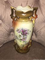 Front view of the antique vase showing hand painted floral decoration on cream background with gradient brown and gold tones at top and base.