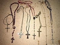 Lot of 8 crosses and rosaries laid out on a beige fabric background, showing various styles and materials including wood, metal and beads.
