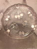 Top view of clear glass round platter featuring embossed cherry clusters and leaves, showing slight pink tint and scalloped edge.