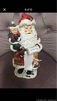 Santa Claus figurine sitting with a child on lap and holding a scroll, showing full front view.