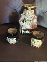 Set of three Toby jugs, one large and two small, showing overall condition and details of ceramic hand-painted faces and attire.
