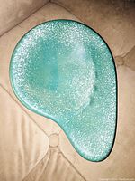 Top view of kidney-shaped teal ceramic ashtray showing white speckled accents