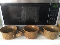 Three vintage ceramic French onion soup bowls in front of microwave, showing size and shape with handles visible