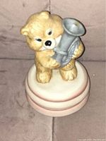 Front view of the bear figurine music box showing the bear holding a silver horn upright on a circular base with pink and white rings.