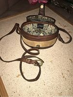 Open top view showing the interior lining of the oval leather box purse and shoulder strap partially laid out.