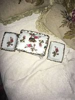 Photo showing the full vanity set – two rectangular trinket trays with floral patterns and a larger footed box with lid, all hand-painted with gold trim and pink rose floral designs on white porcelain.