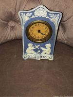 Front view of the vintage blue ceramic wind-up alarm clock showing clock face with classical relief design