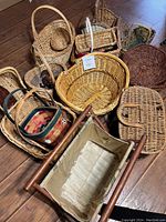 Photo showing 13 assorted woven baskets on wooden floor including oval, round, rectangular shapes with various handles, colors, and weaves.