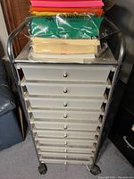 Photo shows a white plastic organizer with 12 drawers and a stack of assorted color card stock on top.