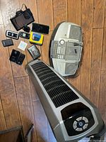 Photo showing entire lot spread on wooden floor with tower fan, boombox, multiple phones, Walkman and chargers.