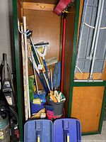 Full view of closet area with cleaning equipment including mops, brooms, duster, bucket with brushes, and ironing board