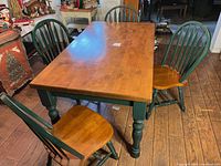 Photo showing the entire dining table with four matching chairs around it, highlighting the green legs and wood top.