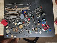 Overview of fashion jewelry items including necklaces, earrings, brooches, pendants, and pins laid out on a black surface
