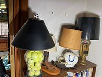 Photo showing four unique lamps: tennis ball filled lamp with black shade, cowboy boot lamp with beige shade, white football helmet lamp, vintage parking meter lamp with black shade