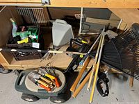 Photo showing multiple garden tools including hand tools, rakes, and a sprayer on a shelf and cart.