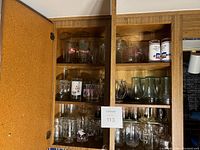 Two wooden cabinets opened showing various clear glassware and three ceramic mugs inside on shelves.