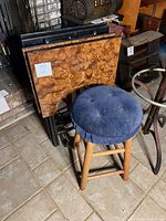 Wooden stool with blue cushioned seat and four portable tables with wood grain patterned tops.