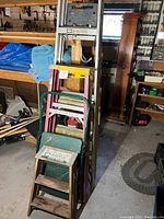 Four ladders stacked inside a workshop environment showing metal, wood, and colored ladders of varying sizes.