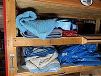Four moving blankets and one blue tarp folded and stacked on wooden shelving unit.