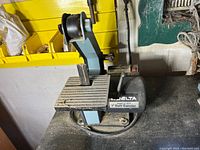 Photo of Delta 1-inch belt sander on a workbench, showing the sanding table, belt assembly, and model label.