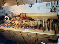Overview of various hand tools spread out on a counter including many screwdrivers, hammers, and some small tools.