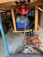 Photo showing the Shop Vac wet/dry vacuum cleaner with hose on the floor, red power tool mounted above, and orange extension cords nearby.