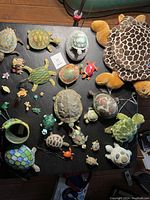 Overview of turtle figurines and plush toys on black table including large plush turtle and diverse small turtle decorations.