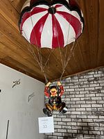 Clown figurine wearing orange and black with red and white parachute hanging from ceiling