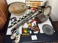 Overview of lot with all items on table including rustic wooden bowl, Radio Flyer wagon, jewelry box, reindeer bells on leather straps, brass pitcher, metal dish, baby shoes, horseshoe, wooden toys, and Jamaica plaque.