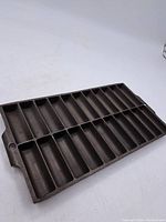 Full view of the dark seasoned cast iron bread stick pan showing 12 rectangular bread stick molds arranged side by side with a handle on one end.