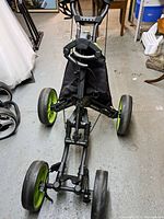 Overall view of the CaddyTek golf caddy showing black frame, four wheels with green rims, and fabric bag holder.