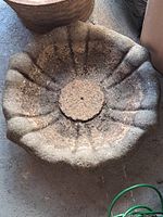 Top view of circular concrete bird bath top showing petal-like design and central hole in heavily used condition.