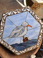 Octagonal garden pad top with a stained glass seagull mosaic showing colors of white, gray, blue, and orange with geometric border detail.