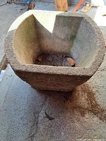 Overhead and interior view of worn square concrete planter showing thickness and rough interior surface with some debris inside.