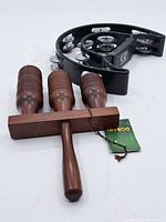 Black plastic tambourine with six pairs of metal jingles arranged around the frame and Dobani logo on the handle. Wooden percussion instrument with three hollow wooden tubes with ridged grooves.
