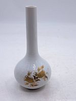 Full view of white porcelain vase with bulbous base and tall slender neck showing embossed pattern and gold floral design on one side.