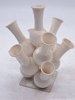 View from slightly above showing seven cream-colored plastic vase necks arranged in cluster on a square base.
