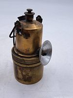 Side view of vintage brass miner's lamp showing cylindrical shape, metal reflector, and hook.
