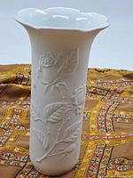 Front view of vintage Kaiser white porcelain vase showing embossed rose and leaf decoration on flared body with scalloped rim.