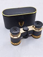 View of Menon vintage opera glasses in front of black leather case with gold trim and clasp